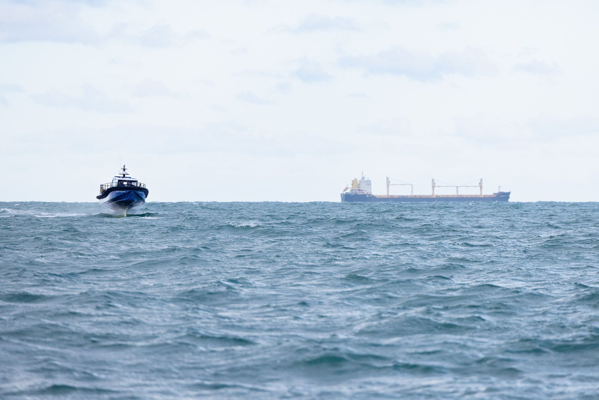 Pioneer of Belfast blue boat foiling through the waves away from the ship in the background