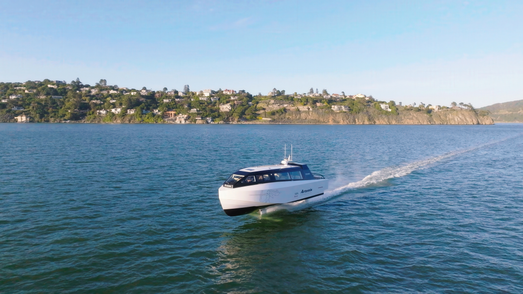 A white boat hydrofoiling above the water with an island in the background