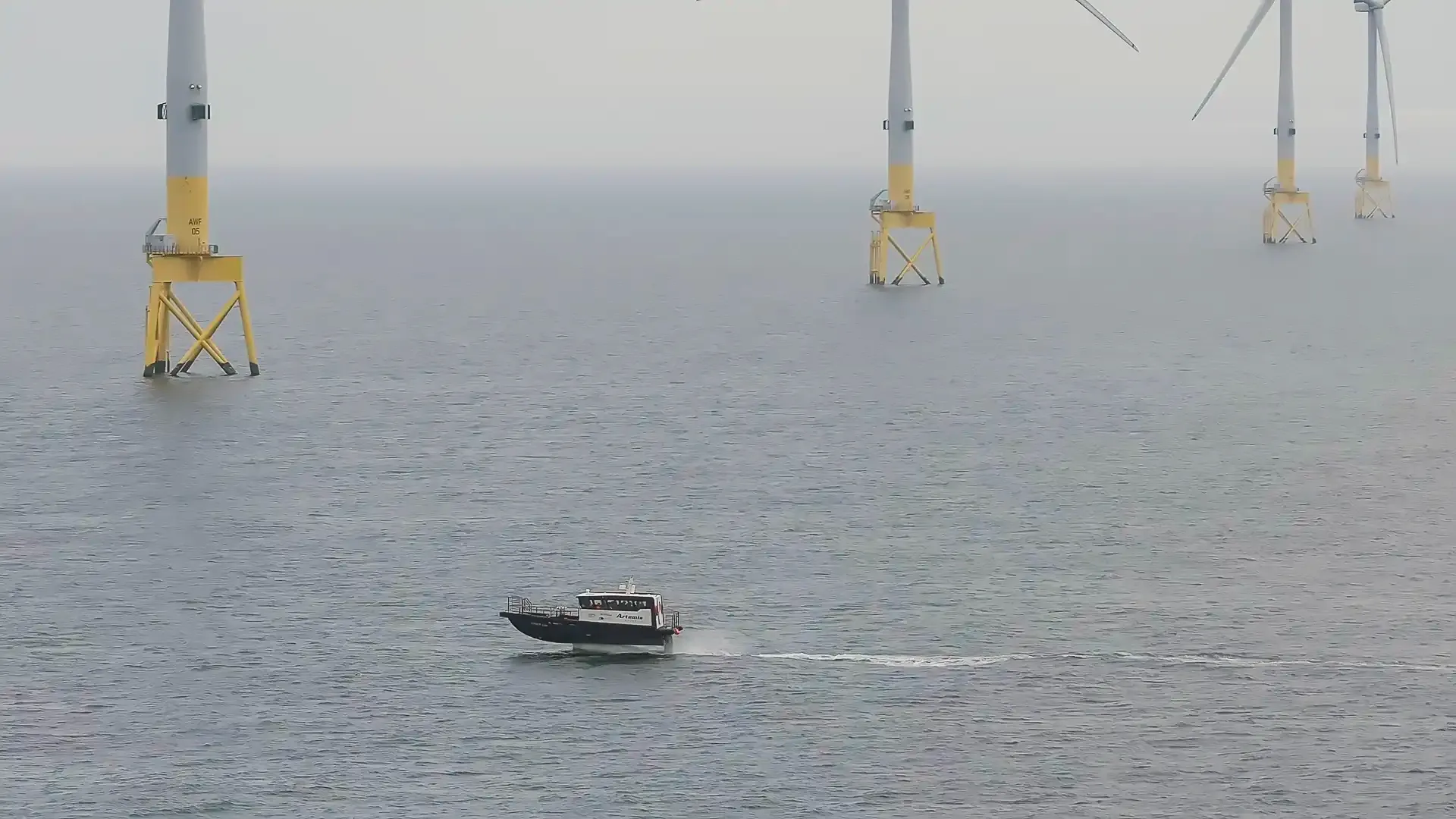 Offshore wind turbines in the distance and the electric foiling crew transfer vessel in the foreground foiling 