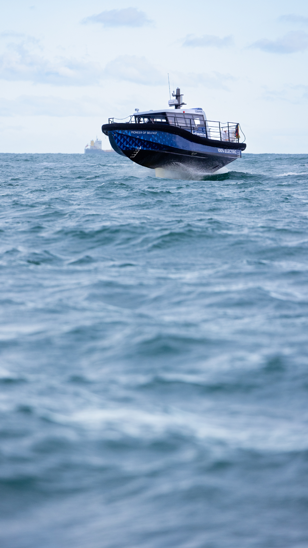 A blue foiling workboat in the sea with a ship in the background