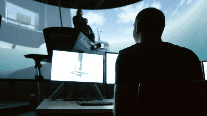 Man sitting at computer screens Infront of Artemis Technologies Simulator