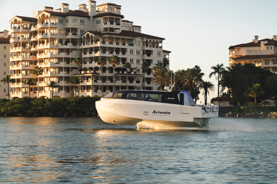 White boat foiling above water with buildings and palm trees in the background