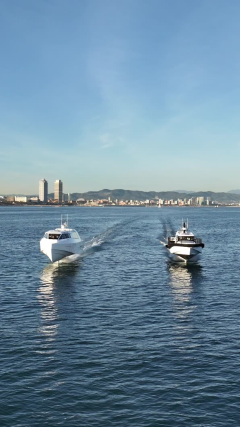 Artemis EF-12 Escape luxury white water taxi foiling alongside a white Artemis EF-12 Workboat with  Barcelona in the background