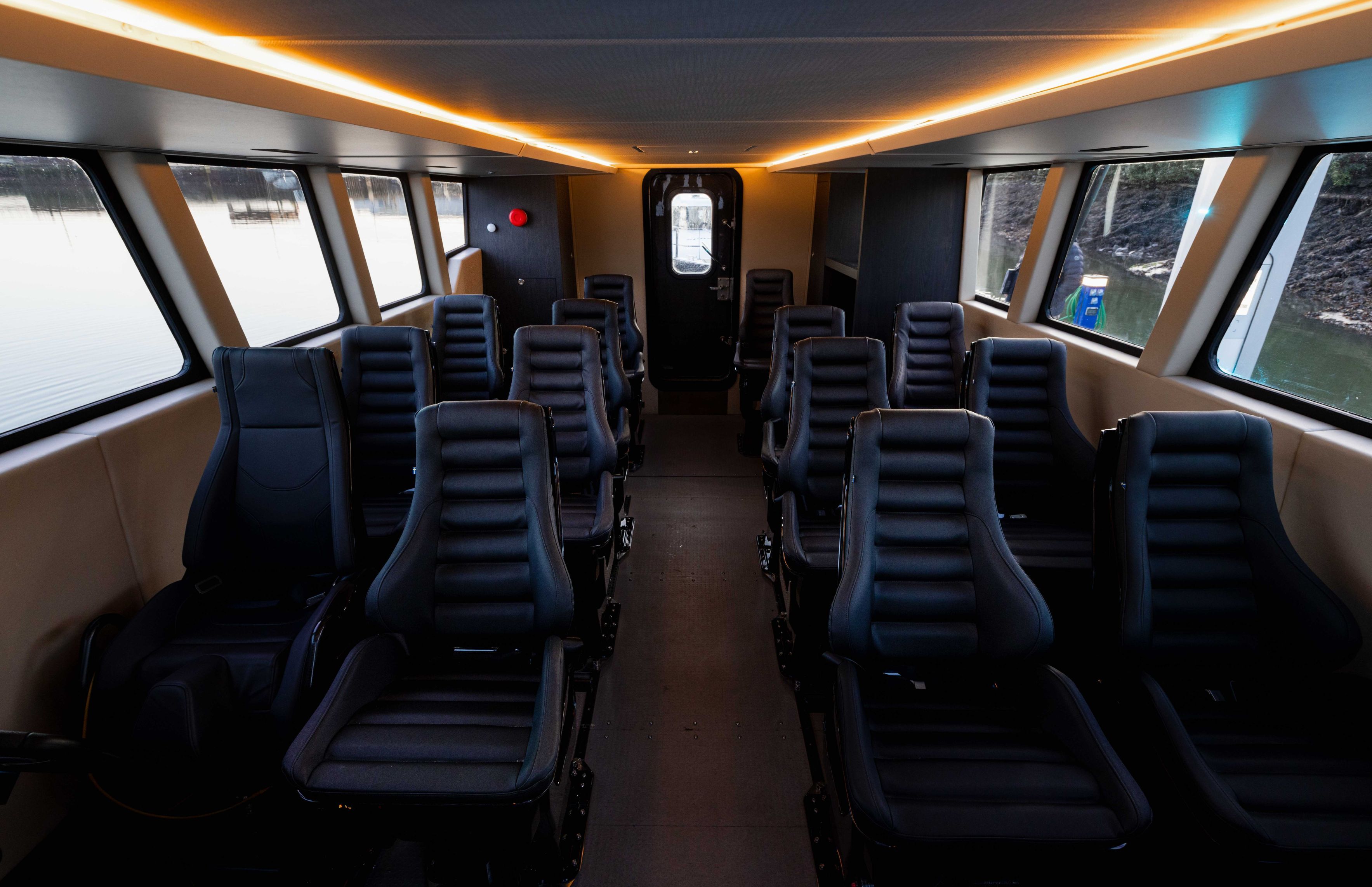 Showing 12 black seat, a central isle with lights on the ceiling following the line of the isle to the back door of the vessel