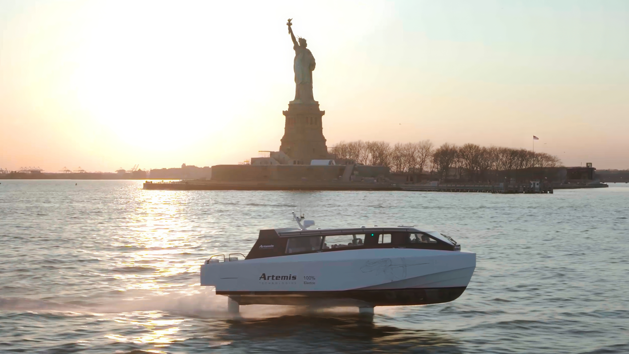 A hydrofoil boat in front of the Statue of Liberty at sunset